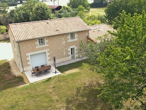 Un bâtiment à deux étages, doté d’un toit recouvert de tuiles, d’un garage et d’une terrasse aménagée avec du mobilier d’extérieur.