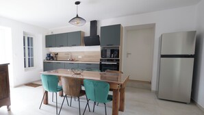 Una cocina moderna con una isla central, dos sillas color turquesa, un refrigerador de acero inoxidable y una lámpara colgante.