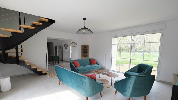 Una sala de estar moderna con sillas color turquesa, una mesa de centro de madera y una escalera.