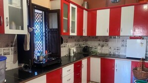 A kitchen with red and white cabinets, a black countertop, and a tiled backsplash. - Shanti Kunj Home Stay (Pauri)