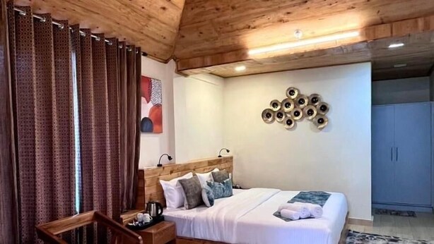 A wooden ceiling with a sloped design, a bed with a wooden headboard, a red chair, and a patterned curtain. - Shanti Kunj Home Stay (Pauri)
