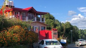 A two-story house with a red roof and balcony, surrounded by orange flowers and greenery. - Shanti Kunj Home Stay (Pauri)