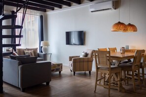 Ein modernes Wohnzimmer mit Sofa, Sesseln, einem Esstisch und einem Fernseher.