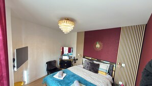 A bedroom with a bed, a TV, a desk, and a chair. - Royal Rose Apartment With Royal Garden (Le Bourget)