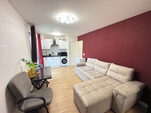 Una sala moderna con un sofá color beige, una mesa de comedor con sillas y una cocina al fondo.