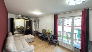 A living room with a sofa, a dining table, and a black wardrobe with a Gucci logo. - Royal Rose Apartment With Royal Garden (Le Bourget)