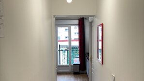 A narrow hallway with a wooden floor, a ceiling light fixture, and a door leading to a balcony. - Royal Rose Apartment With Royal Garden (Le Bourget)