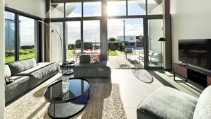 A spacious living room with a large glass door leading to an outdoor patio, a sofa, a coffee table, and a flat-screen TV. - Architect-designed Villa With sea View (Le Conquet)