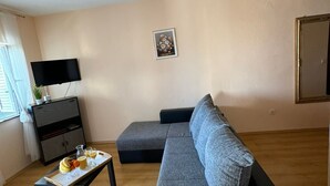 A living room with a grey sofa, a small table with fruits and glasses, a TV, and a picture on the wall. - Beautiful Apartment Bodulo 1 (Povljana)