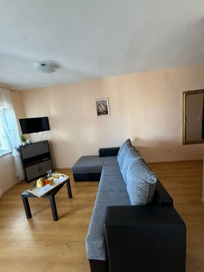 A living room with a grey sofa, a small table with fruits and glasses, a TV, and a picture on the wall. - Beautiful Apartment Bodulo 1 (Povljana)