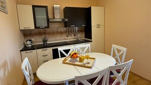 A compact kitchen with white cabinets, a black range hood, and a dining table with four white chairs. - Beautiful Apartment Bodulo 1 (Povljana)