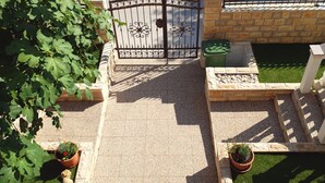 A gated entrance with a decorative iron gate, potted plants, and a paved pathway leading to a building. - Beautiful Apartment Bodulo 1 (Povljana)