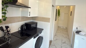 A modern kitchen with a black countertop, a washing machine, and a compact refrigerator. - Royal Sapphire Apartment With Royal Garden (Le Bourget)