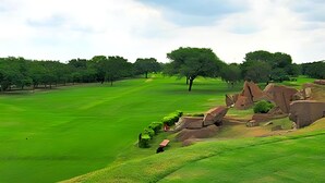 Een golfbaan met een verzorgd gazon, enkele bomen en grote rotsformaties.