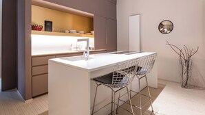A modern kitchen with a white countertop, stainless steel sink, and bar stools. - ARCHILOFT Brera Gae Aulenti Moscova (Milano)