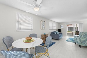 Ein modernes Wohnzimmer mit Essbereich, ausgestattet mit Deckenventilator, einer Couch, einem Couchtisch und einem Fernseher.