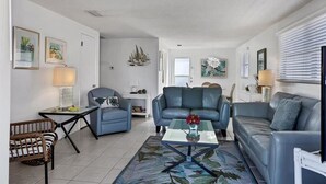 Una sala de estar con un sofá azul, una mesa de centro con un florero y una silla de mimbre.