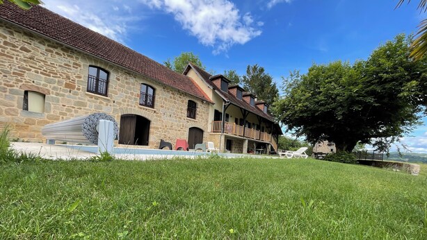A stone building with a tiled roof, a grassy lawn, and a large tree.