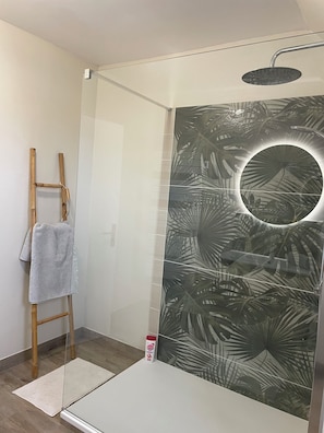 A shower with a circular mirror, a towel rack, and a wooden ladder.