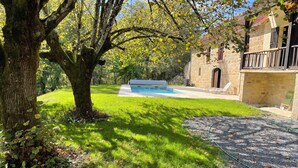 A stone building with a swimming pool, surrounded by a grassy lawn and trees.