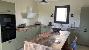 A modern kitchen with green cabinets, a wooden island, a Bosch oven, and a window providing natural light.