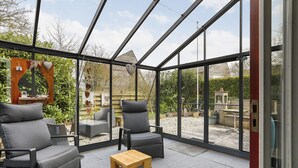 Une véranda avec deux chaises grises, une table en bois et une vue sur un jardin.