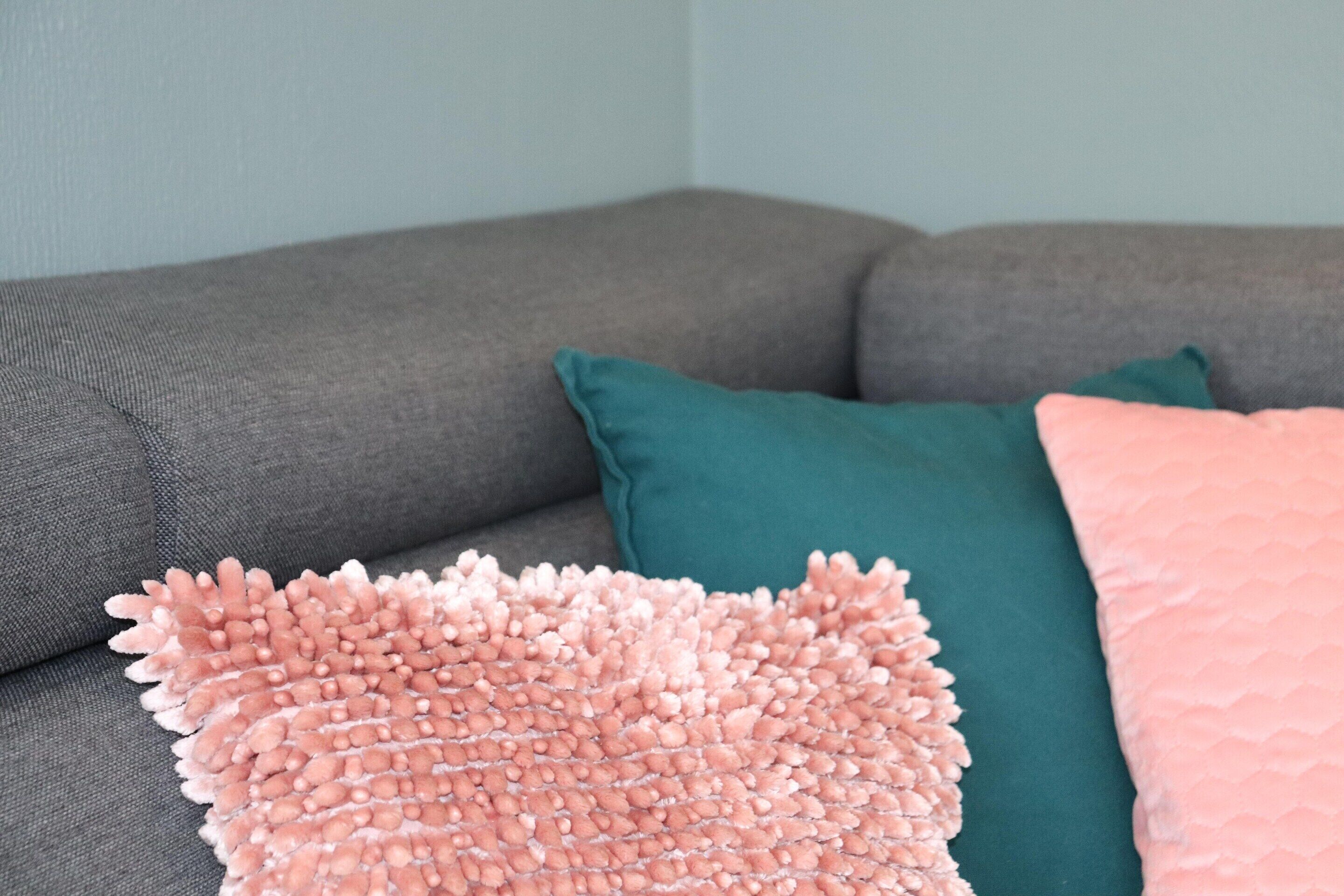 Ein graues Sofa mit türkisen und rosafarbenen Kissen.