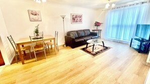 Una sala de estar con piso de madera, un sofá, una mesa de centro, un televisor y un comedor con sillas y una mesa.
