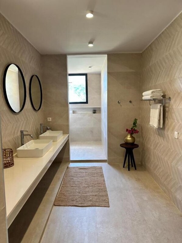 Un baño moderno con dos lavamanos, un espejo grande, una mesita con un florero y un perchero para toallas.