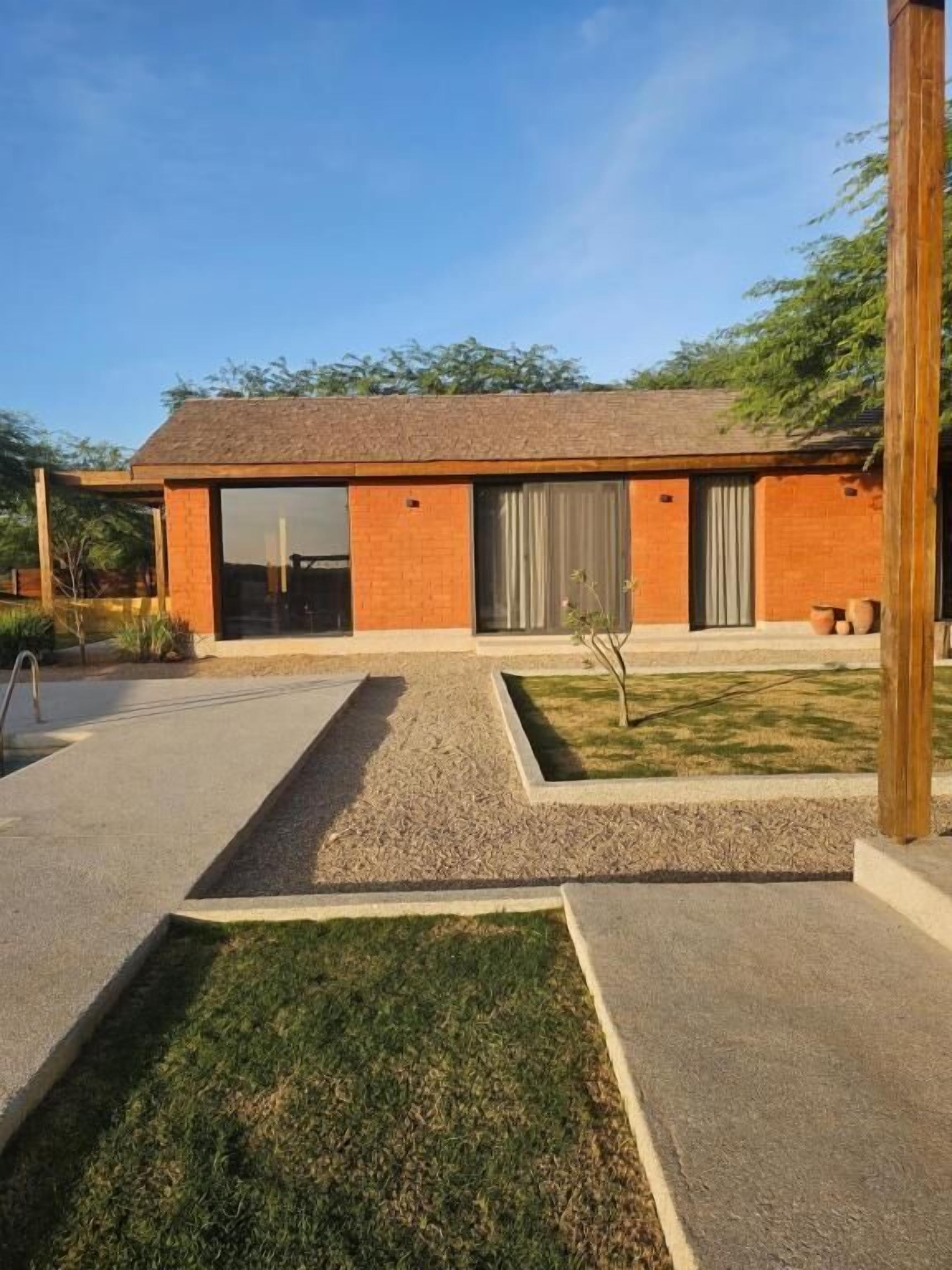 A modern house with a brick exterior, large windows, and a small garden area with a lawn and gravel paths.