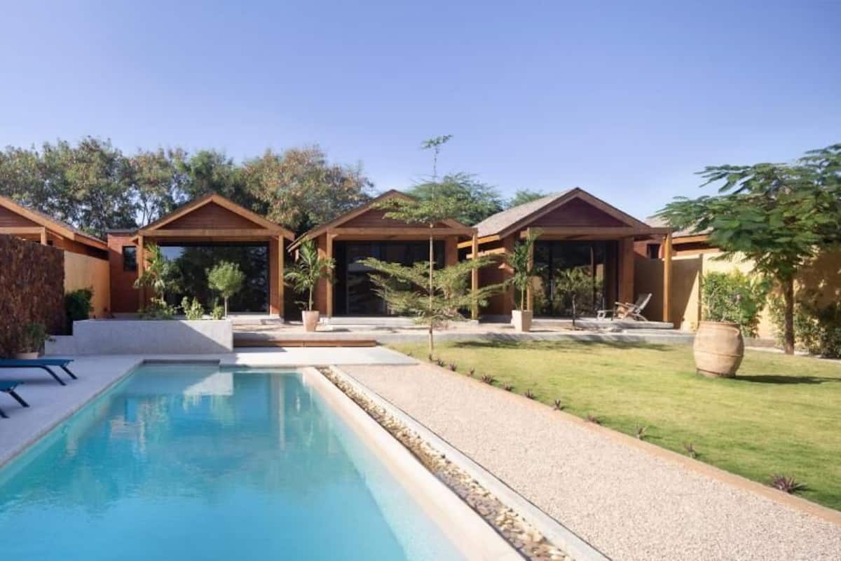 A modern pool area with a clear blue pool, lounge chairs, and wooden structures.