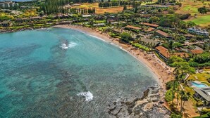 Luftaufnahme eines Küstenresorts mit Strand, klarem Wasser und üppiger Vegetation.