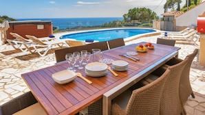 Un área de comedor junto a la piscina con una mesa dispuesta para cuatro, con vistas a una piscina y al mar.