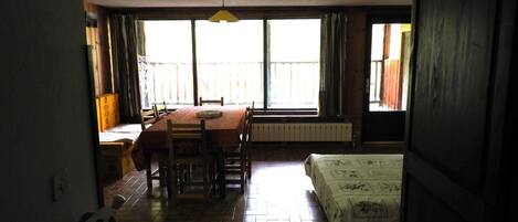 Una habitación con una mesa de comedor y sillas, una cama, un radiador y ventanas amplias.