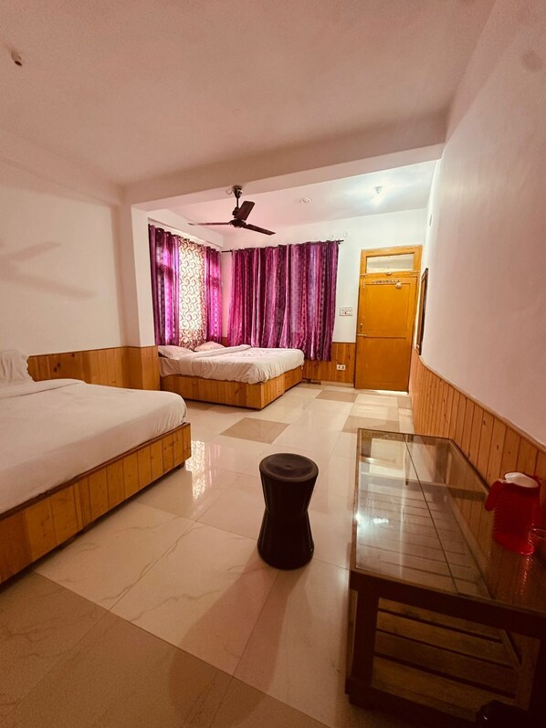 A hotel room with two beds, a ceiling fan, a wooden bench, and a glass table. - The Aston hills kasol (Bhuntar)