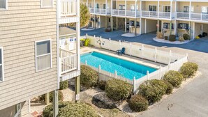 Ein mehrstöckiges Hotel mit Schwimmbecken, umgeben von einem weißen Zaun, und ein Parkplatz davor.