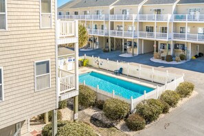 A multi-story hotel with a swimming pool surrounded by a white fence, and a parking area in front. - Shore Thing - 4BR, Dog Friendly, Community Pool, Ocean Views (Surf City)