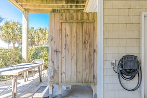 A wooden door with a metal latch, a concrete floor, a white chair, and a hose connected to a wall-mounted electrical outlet. - Shore Thing - 4BR, Dog Friendly, Community Pool, Ocean Views (Surf City)