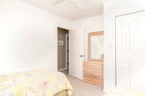 A bedroom with a bed, a dresser, a mirror, and a door leading to another room. - Serenity Hearts - Oceanfront Serenity Point Home - 2BR! (Topsail Beach)