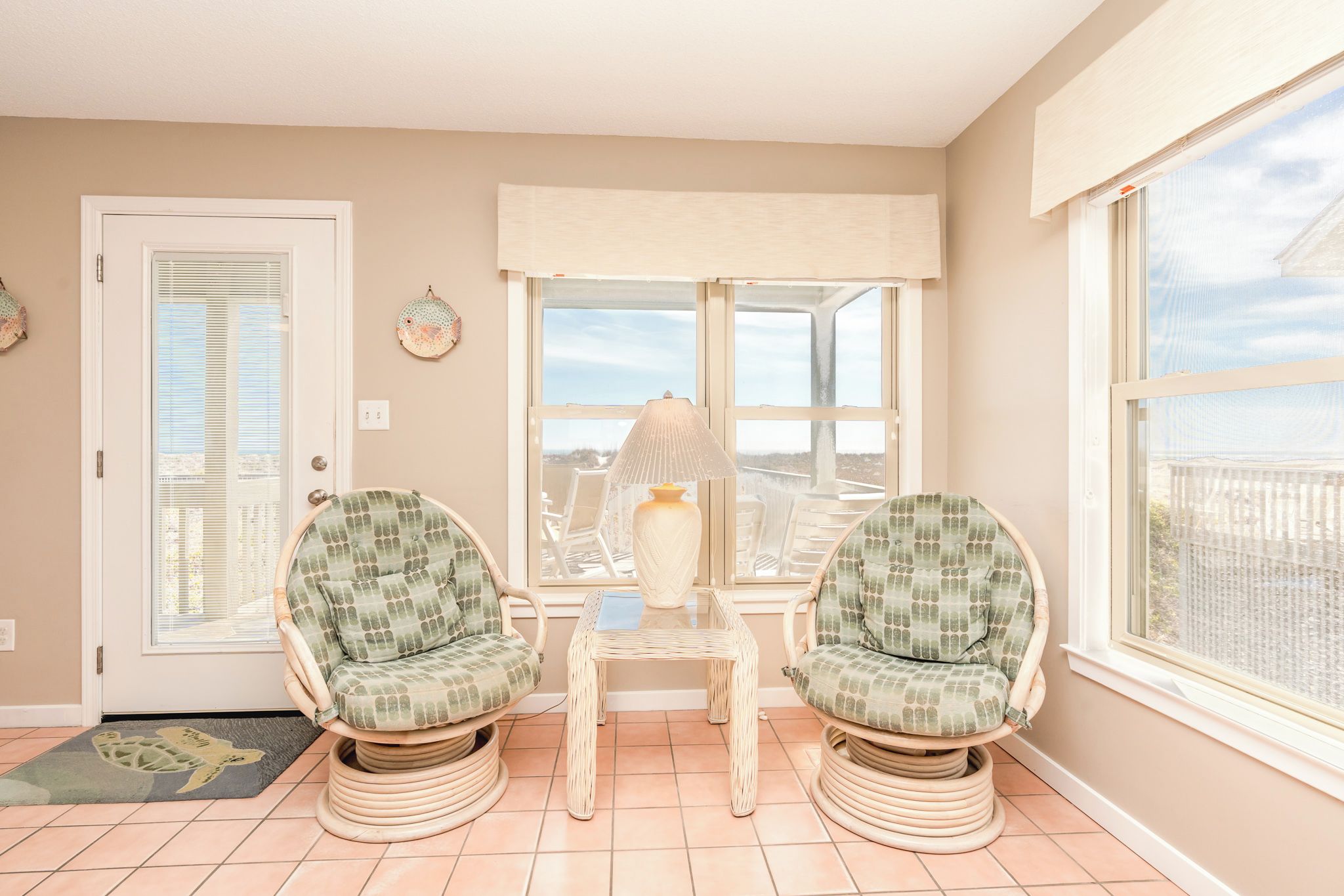 A room with two wicker chairs, a small table, a door, and large windows.