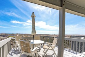 A covered outdoor seating area with a table and chairs, an umbrella, and a view of the landscape. - Serenity Hearts - Oceanfront Serenity Point Home - 2BR! (Topsail Beach)