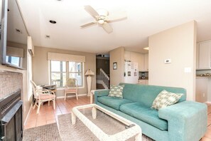 A living room with a sofa, a coffee table, a fireplace, and a dining area with chairs. - Serenity Hearts - Oceanfront Serenity Point Home - 2BR! (Topsail Beach)