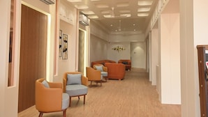 A hallway with modern furniture, including orange sofas and checkered chairs, and a ceiling with recessed lighting. - Hotel Camel managed by CLAY (Mundra)
