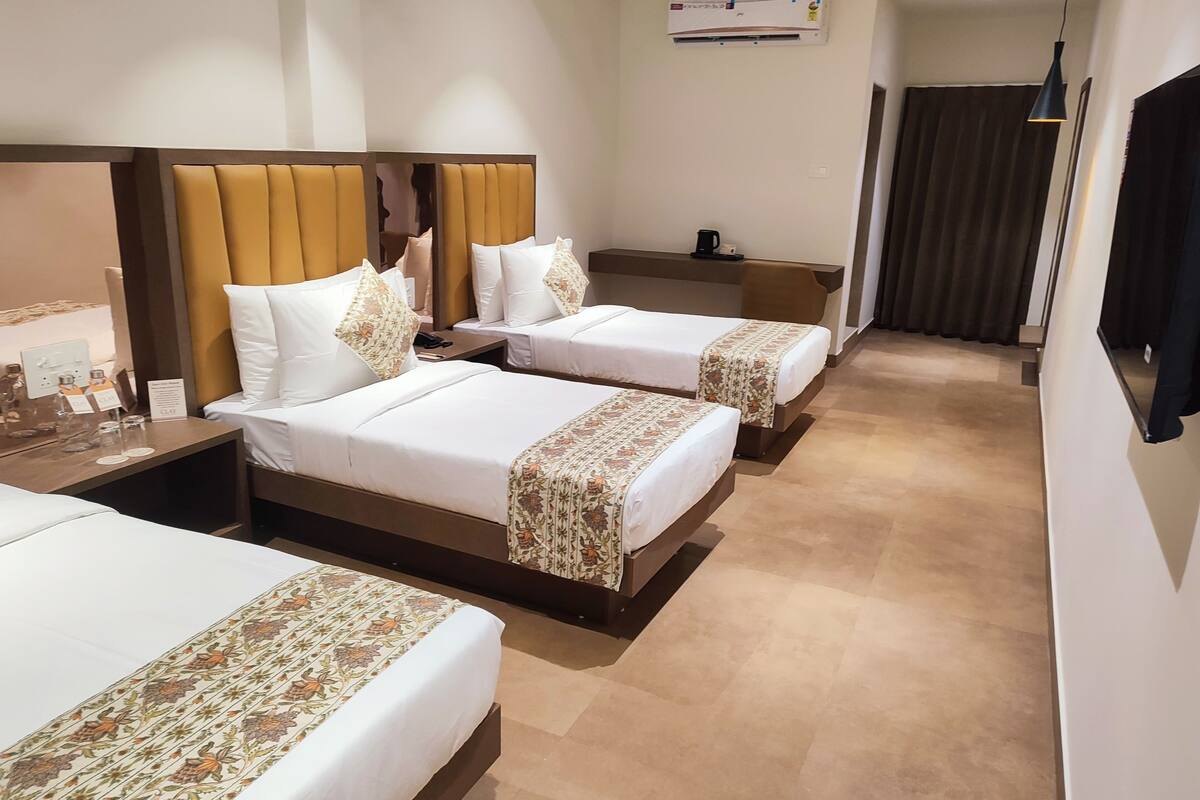 Ein Hotelzimmer mit zwei Betten, einem Nachttisch mit Telefon und Lampe, einer Klimaanlage an der Wand und einem dunklen Vorhang am Fenster.