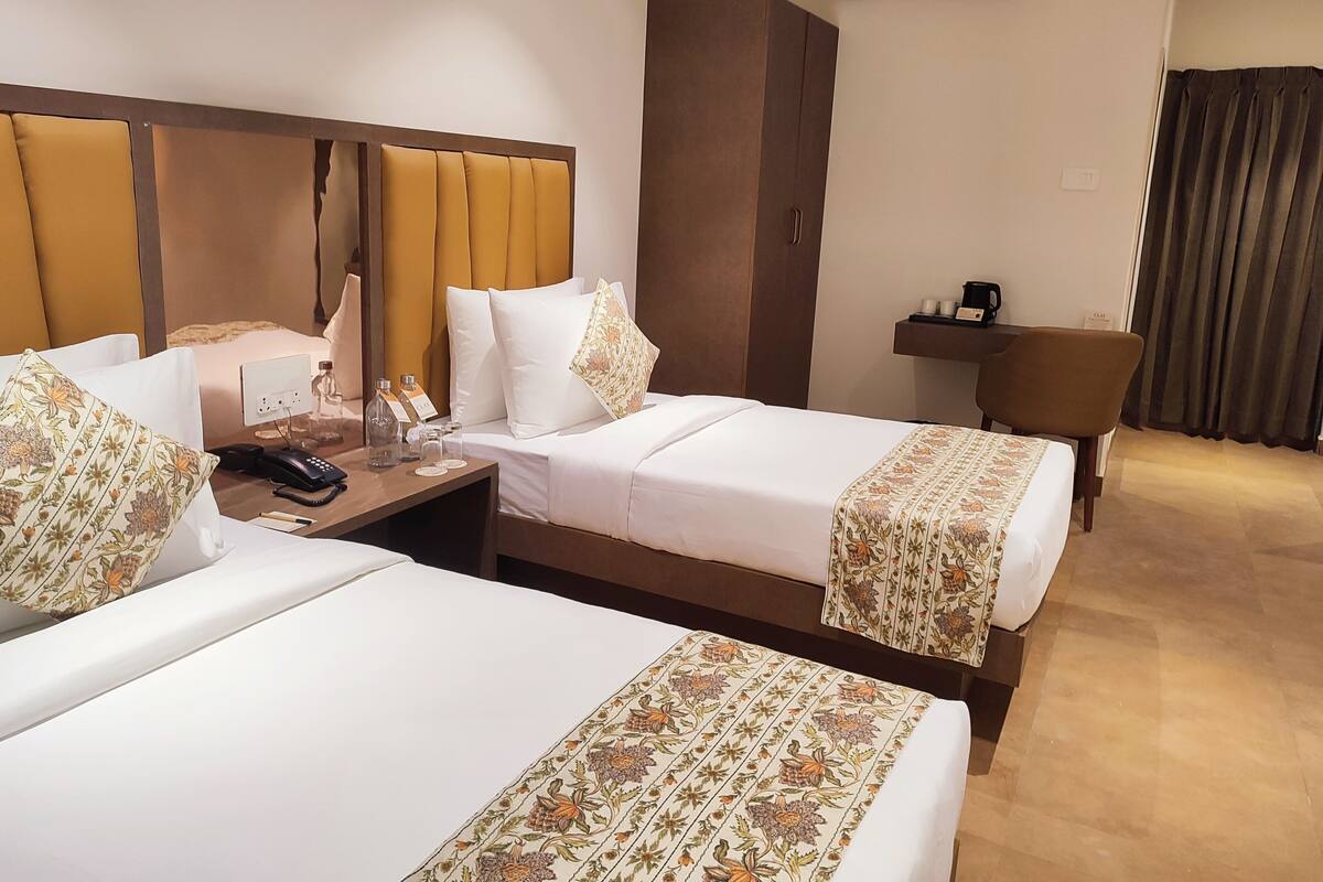 Ein Hotelzimmer mit zwei Betten, einem Schreibtisch mit Telefon und Pflegeartikeln, einem Kleiderschrank und einer Klimaanlage.