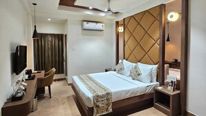 A modern hotel room with a large bed, a desk, a chair, a TV, and a ceiling fan. - Hotel Camel managed by CLAY (Mundra)