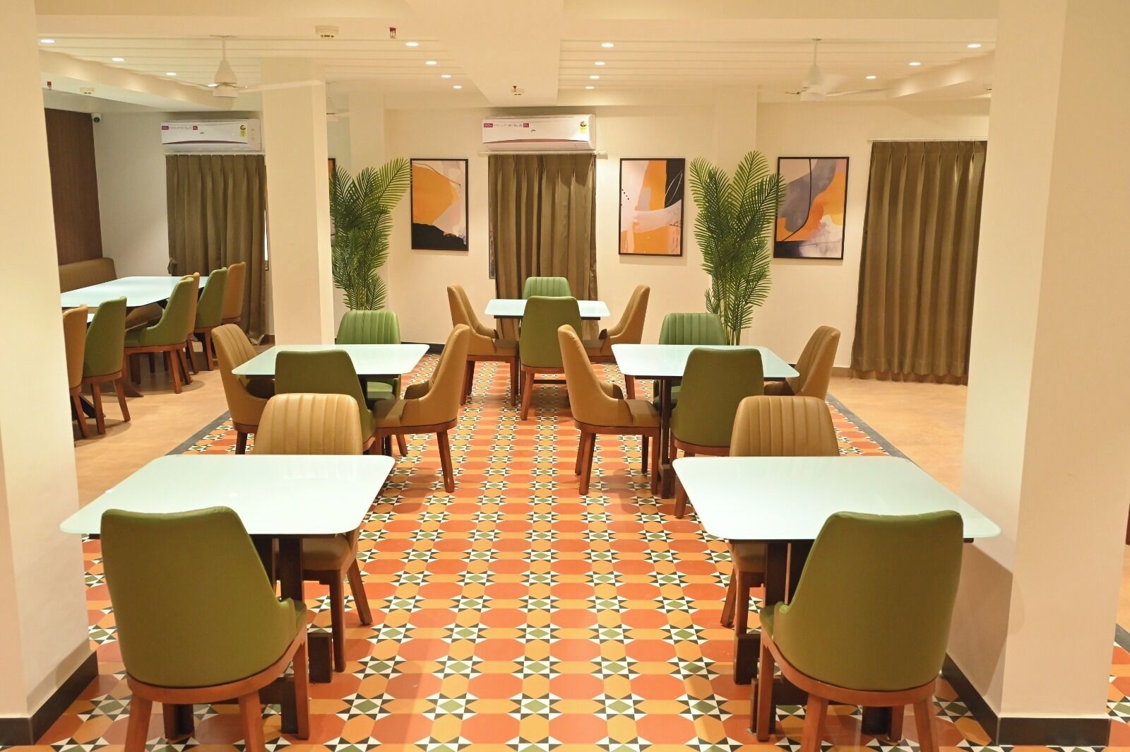 Comedor de hotel con varias mesas y sillas, unidades de aire acondicionado y plantas decorativas.