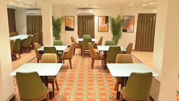 Comedor de hotel con varias mesas y sillas, unidades de aire acondicionado y plantas decorativas.