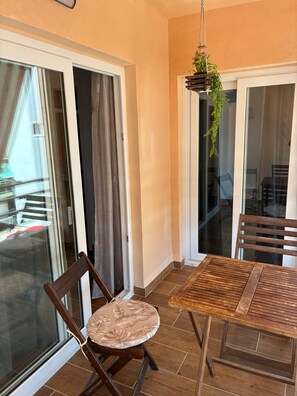 En balkon med et træbord og stole, en hængende plante og skydedøre i glas.