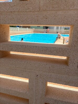 A pool area with a view through a concrete structure, including a pool and a person in the water. - Apartment on the beach. 10 minutes from Valencia Sleeps 4. 2 bedroom 1 bathroom (Playa Puebla de Farnals)